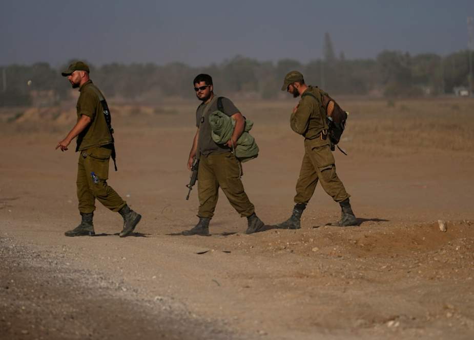 Israeli soldiers walk through a staging area for tanks near the Gaza border