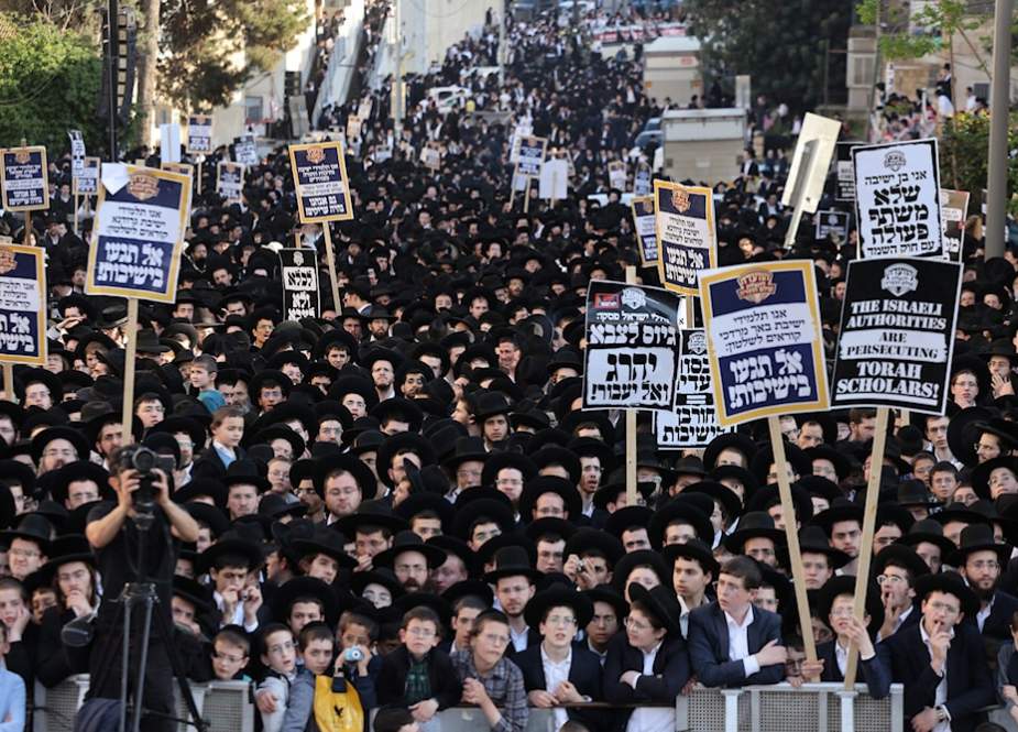 Ultra-Orthodox Jewish men and youth raise placards during a protest against Israeli army conscription outside an army recruitment office in al-Quds