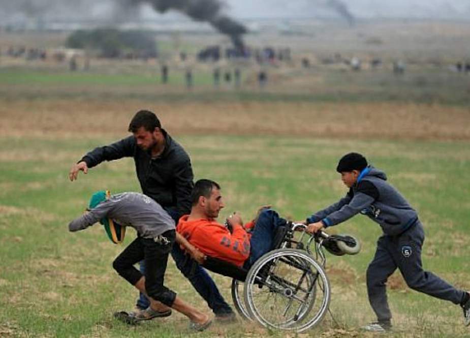 Palestinians-help-a-disabled-man-during-confrontations-with-IOF-near-the-Gaza-border