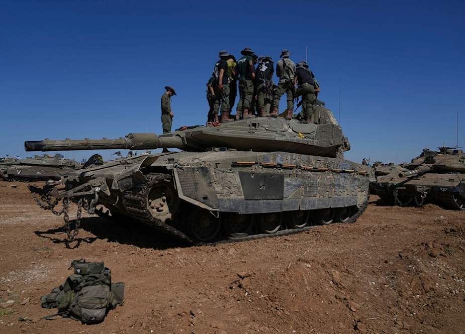 Israeli occupation soldiers repair a tank at a staging ground outside the Gaza Strip, in occupied Palestine
